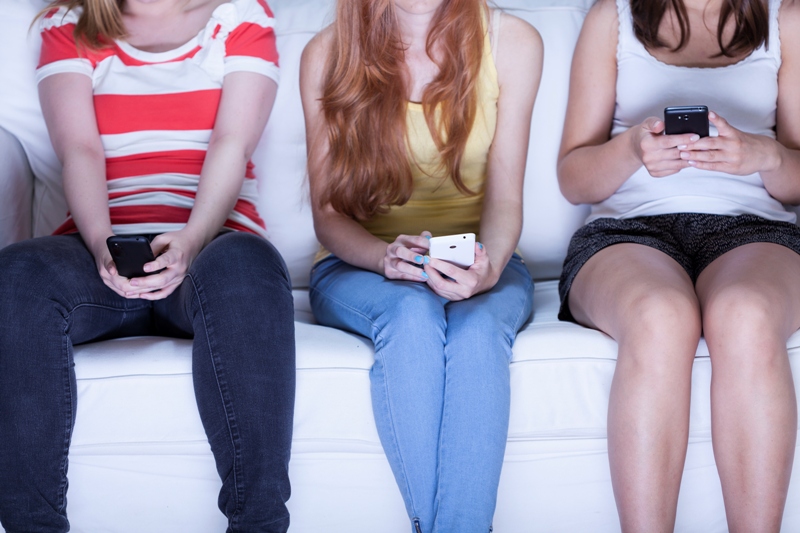 Friends sitting on sofa and using phones