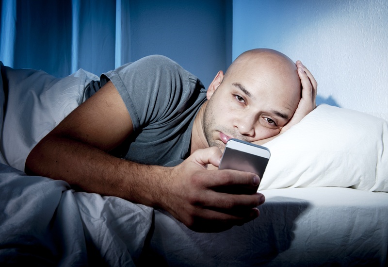 young cell phone addict man awake at night in bed using smartphone